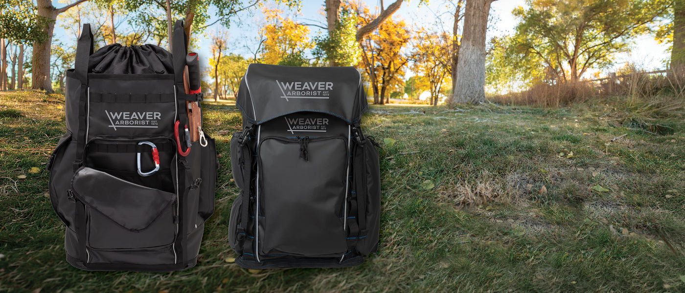 Two black Weaver Arborist gear bags displayed outdoors on grass with trees in the background.